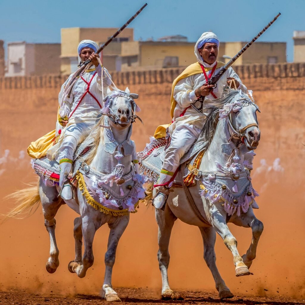 Horsemen in traditional attire performing at a Fantasia event, showcasing horsemanship skills.